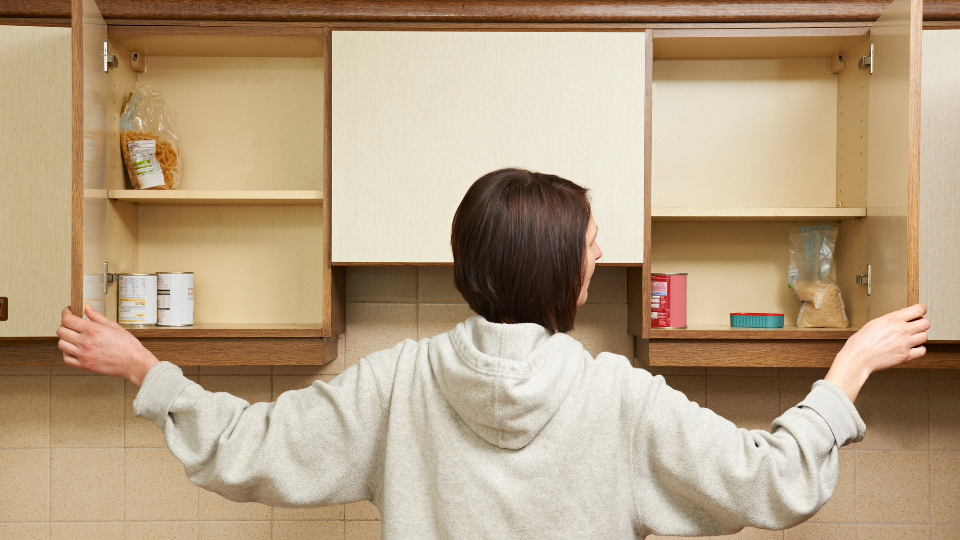 woman looking through empty food cupboards